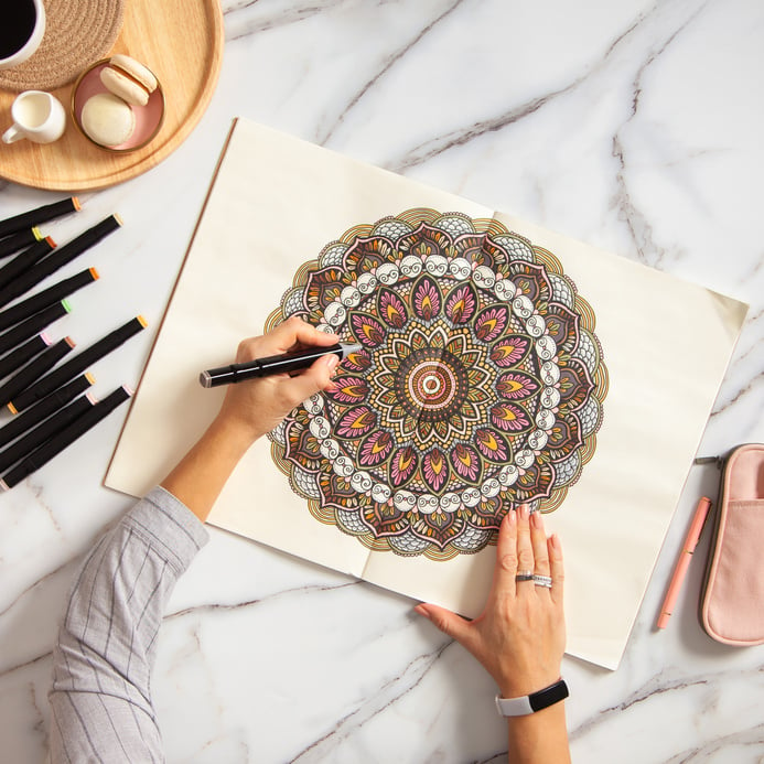 Woman drawing and coloring mandala in sketchbooks with colorful markers while having a breakfast